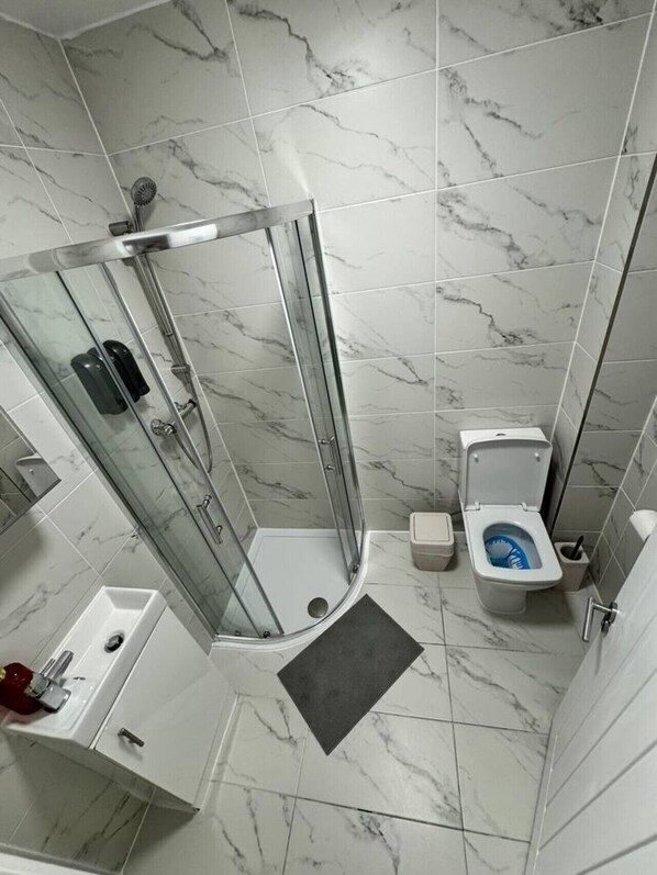 Un baño con ducha de vidrio, inodoro y lavamanos.
