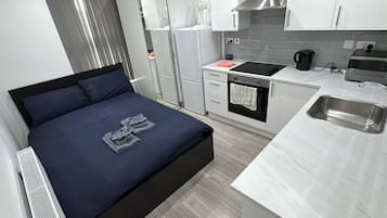 A compact hotel room with a bed, kitchenette, and a small bathroom.