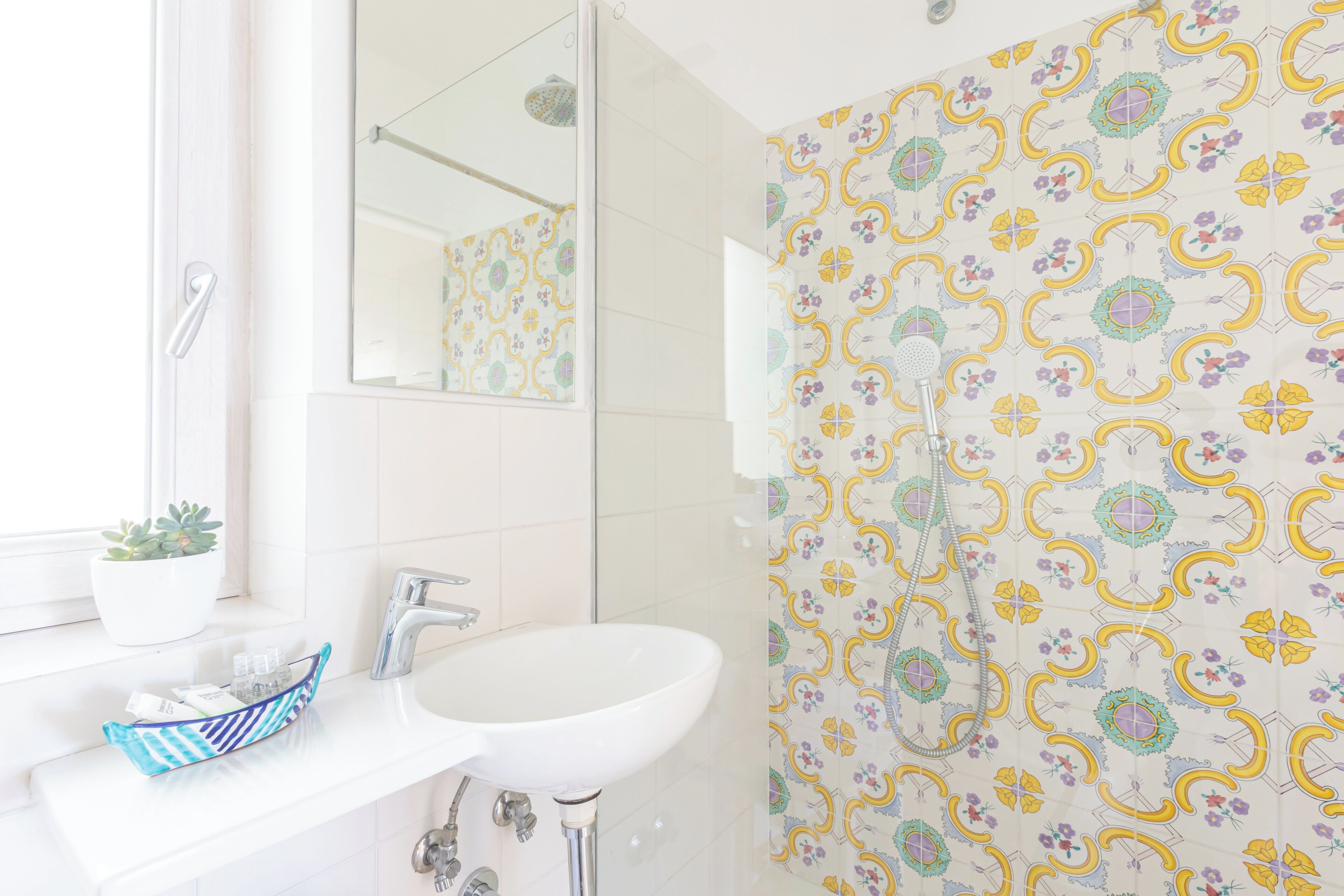 A bathroom with a white sink, a mirror, a potted plant, and a shower with patterned tiles.