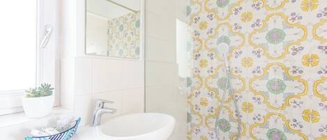 A bathroom with a white sink, a mirror, a potted plant, and a shower with patterned tiles.