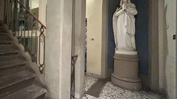 Un escalier orné de rampes en métal travaillées mène à un couloir où se trouve une statue.