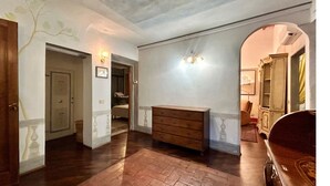 Un couloir doté d’un plancher en bois, d’une commode en bois et d’un lustre.