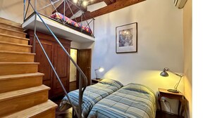 Une chambre avec un escalier en bois, un lit superposé, une table de chevet avec une lampe et un tableau encadré au mur.