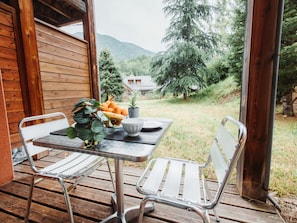 A wooden cabin with a table and two chairs on a deck, overlooking a forested area with mountains in the background. - Cozy 2-bedroom Air-conditioned Apartment (Ax-les-Thermes)