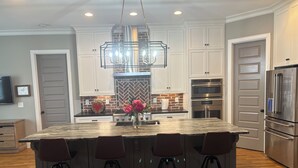 Una cocina moderna con una isla grande, taburetes de bar, electrodomésticos de acero inoxidable y un salpicadero decorativo.