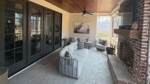 Un patio cubierto con un sofá blanco, sillas de mimbre, un ventilador de techo y una chimenea de ladrillo.