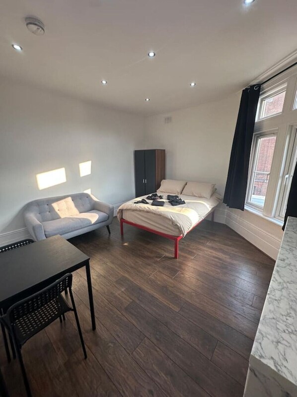 A bedroom with a bed, a sofa, a wardrobe, a table, and a window. - London Clapham Common Room (Greater London)