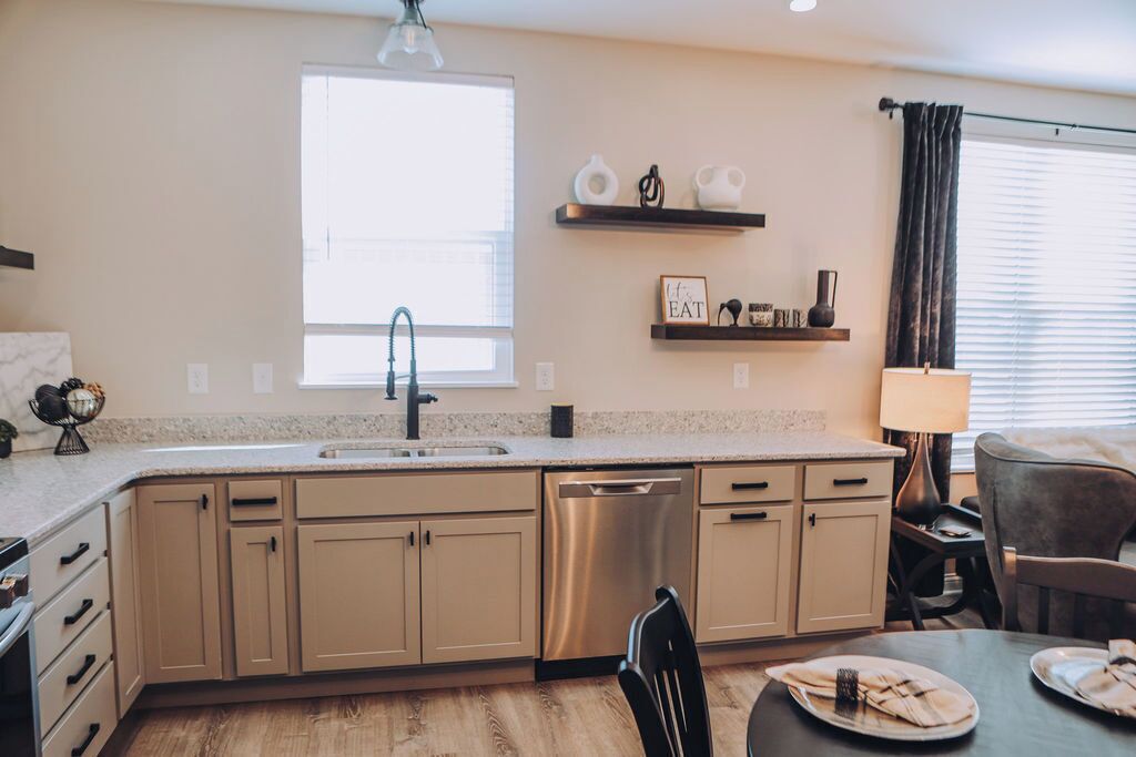 A modern kitchen with a large window, built-in dishwasher, and a dining area with a table set for two.