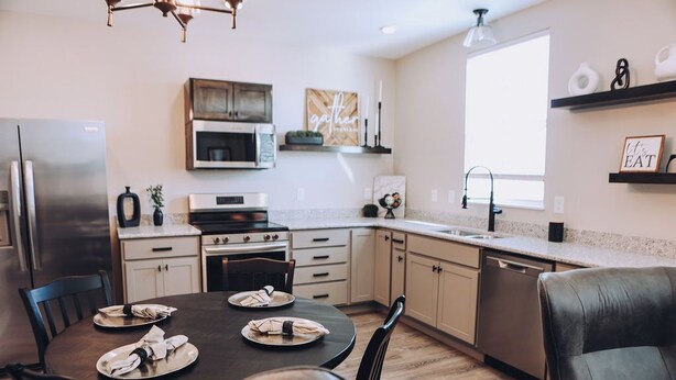 A modern kitchen with a dining area, featuring a stainless steel refrigerator, a microwave, a stove, and a dishwasher.