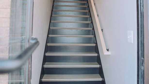 A staircase leading to an upper floor, with a handrail on the right and a glass door on the left.