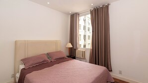 Ein Schlafzimmer mit einem Bett, einem Nachttisch mit Lampe, einem Fenster mit Vorhängen und einer Heizung.