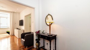 Ein Zimmer mit Holzboden, einem schwarzen Sofa, einem kleinen Tisch mit Lampe und einem Fernseher auf einem Schrank.