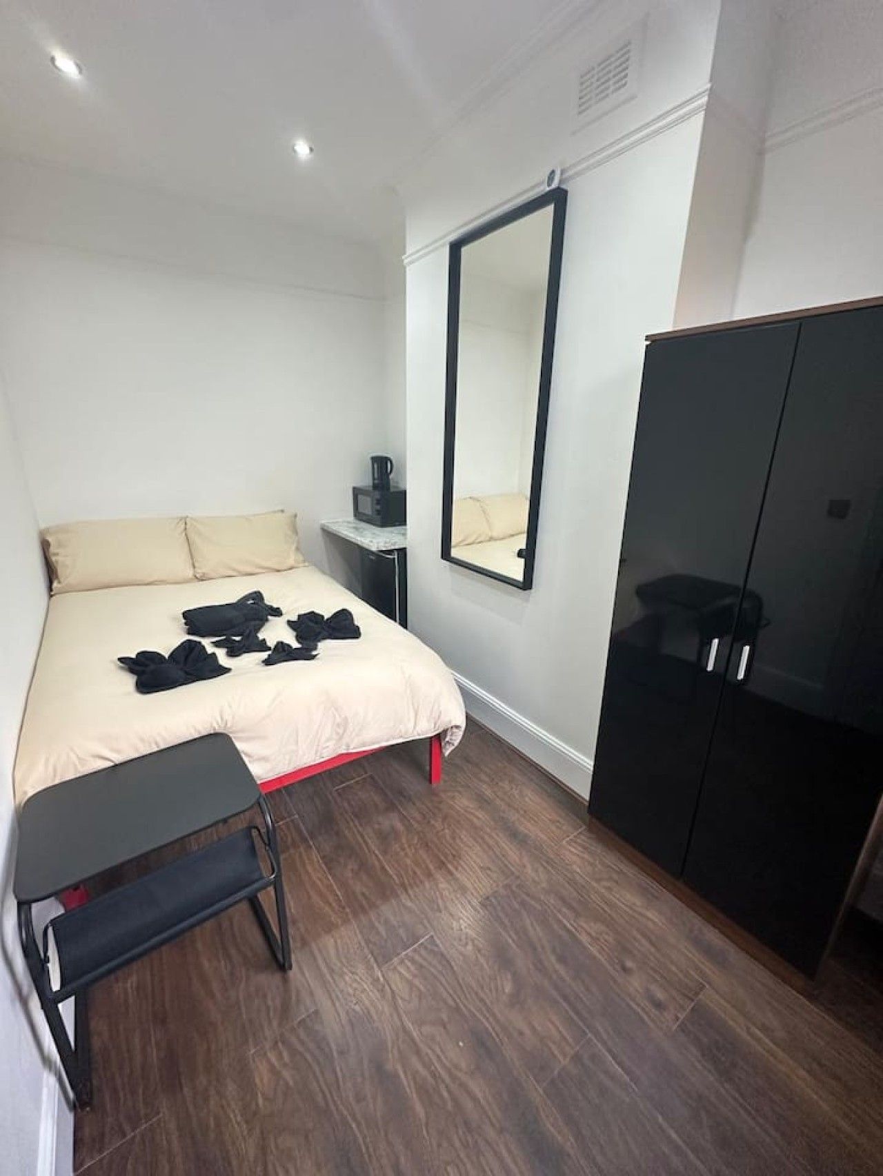 Un dormitorio con cama, mesita de noche, espejo, armario y un pequeño banco.
