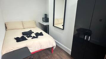 Un dormitorio con cama, mesita de noche, espejo, armario y un pequeño banco.