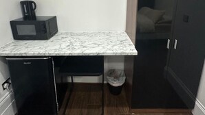 Ein kompakter Raum mit Marmorplatte, einem kleinen schwarzen Kühlschrank, einer Mikrowelle und einem Schrank mit Spiegel.
