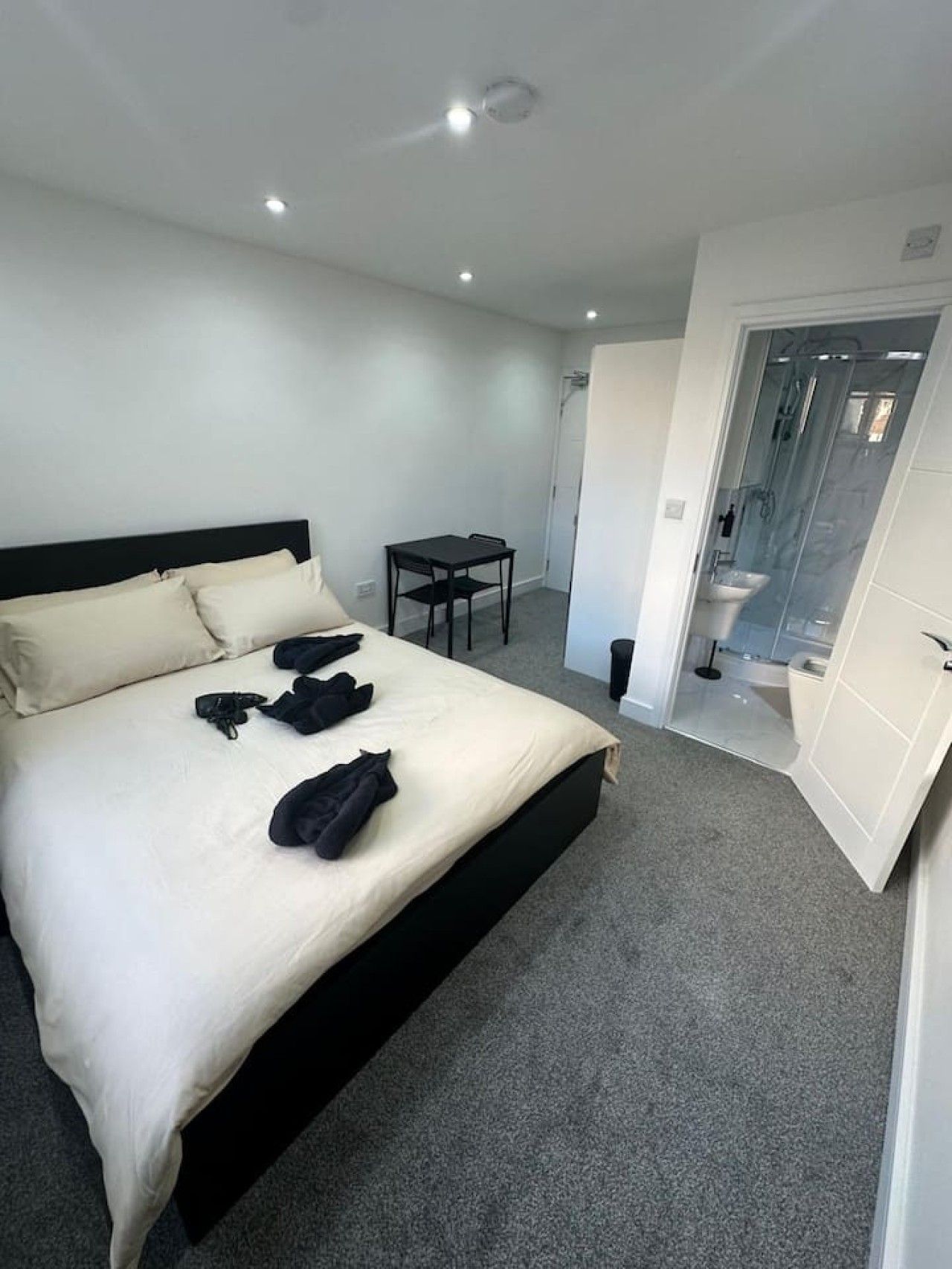 A hotel room with a bed, a small table, and a bathroom visible through an open door.
