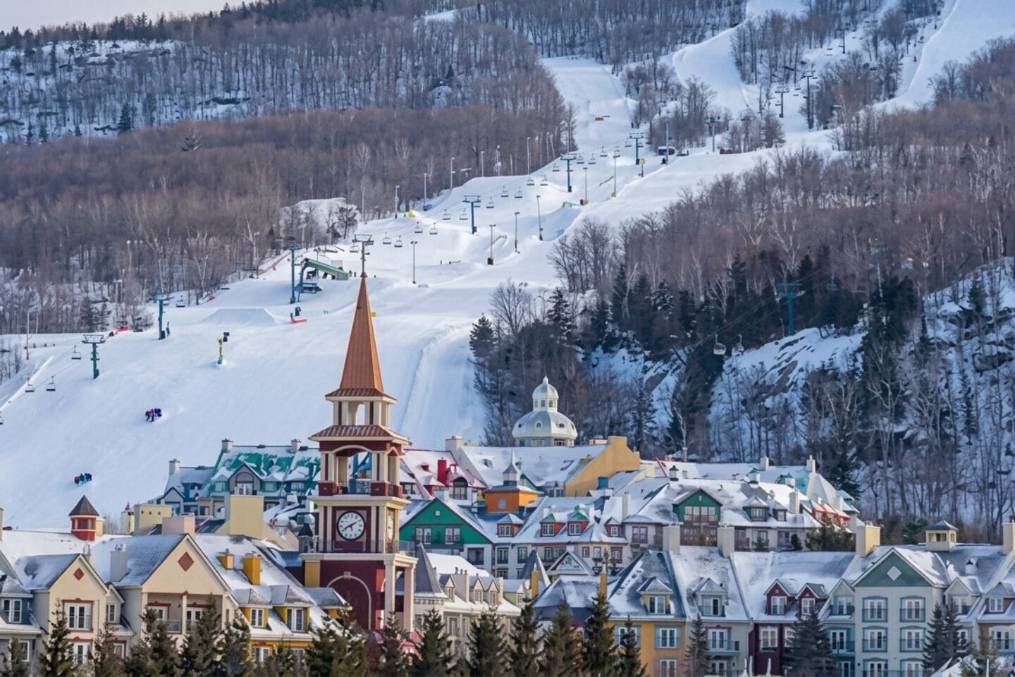 Un pueblo con un campanario de iglesia destacado, edificios coloridos y una pista de esquí nevada.