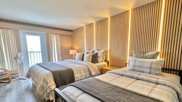Habitación de hotel con dos camas, un balcón, un ventilador y una pared con líneas verticales.