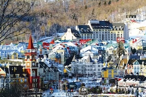 En snötäckt stad med färgglada byggnader, ett imponerande klocktorn och en skidlift i bakgrunden.