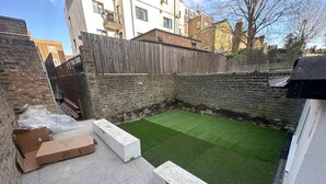 Un patio pequeño con césped artificial, cerca de madera y pared de ladrillo.