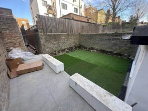 A small backyard with artificial grass, a wooden fence, and a brick wall.