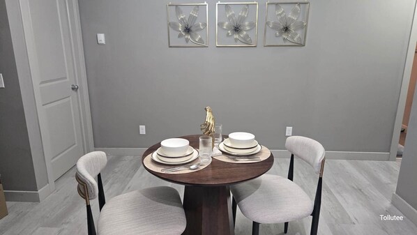 Un coin repas avec une table ronde dressée pour quatre personnes, agrémentée d’assiettes blanches, de couverts et d’un centre de table décoratif.
