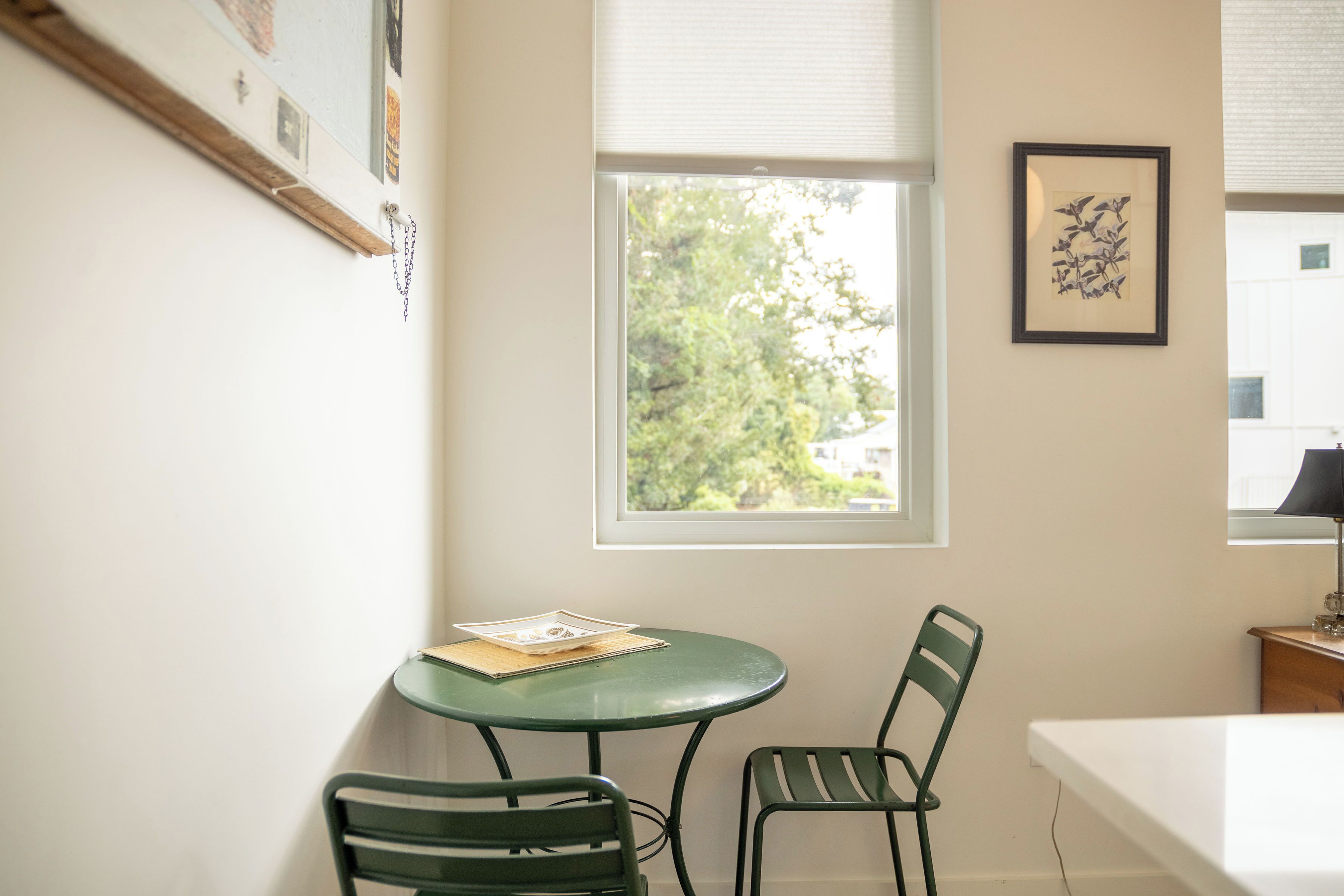 A small room with a round table, two chairs, a window with blinds, and a framed picture on the wall.