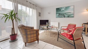 Una sala de estar con un sofá, una silla, un televisor, una planta y un cuadro en la pared.