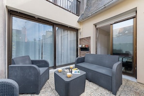 A patio area with a sofa, armchair, and coffee table, featuring a sliding glass door and a view of the street. - Charming Apartment in the Heart of the Artists’ District (Camaret-sur-Mer)