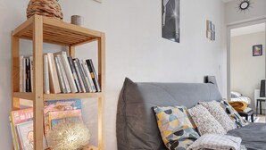 Un dormitorio con un sofá gris, almohadones estampados, una estantería de madera con libros y un globo decorativo.