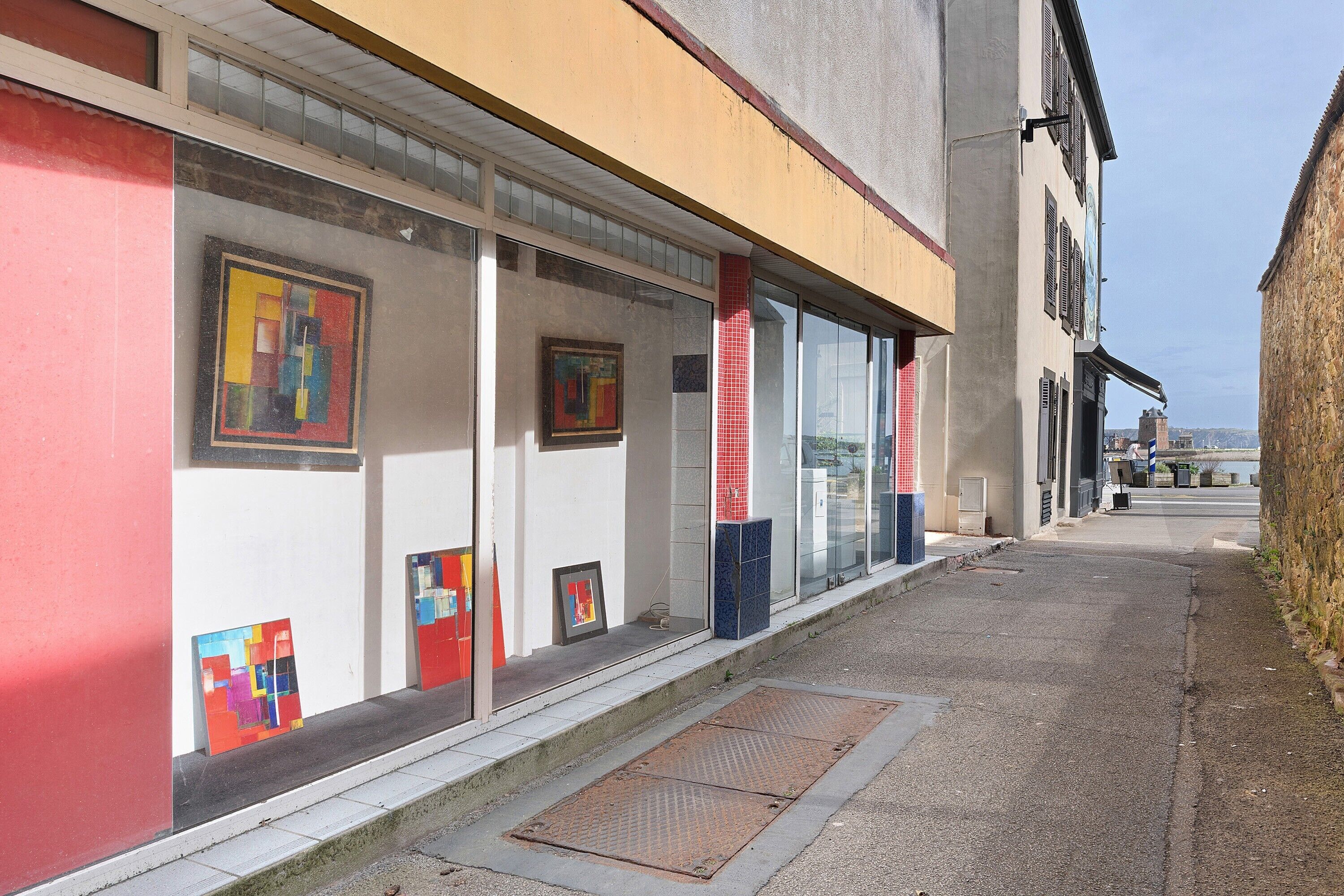 A building with large windows displaying artwork, a sidewalk, and a metal grate.