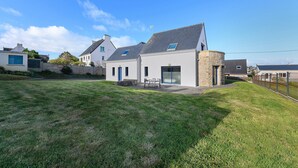 A modern house with a well-maintained lawn, a patio with outdoor furniture, and a stone wall. - Comfortable, Cozy Apartment in Camaret (Camaret-sur-Mer)