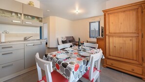 A dining area with a table set for four, a kitchen with modern appliances, and a large wooden cabinet. - Comfortable, Cozy Apartment in Camaret (Camaret-sur-Mer)