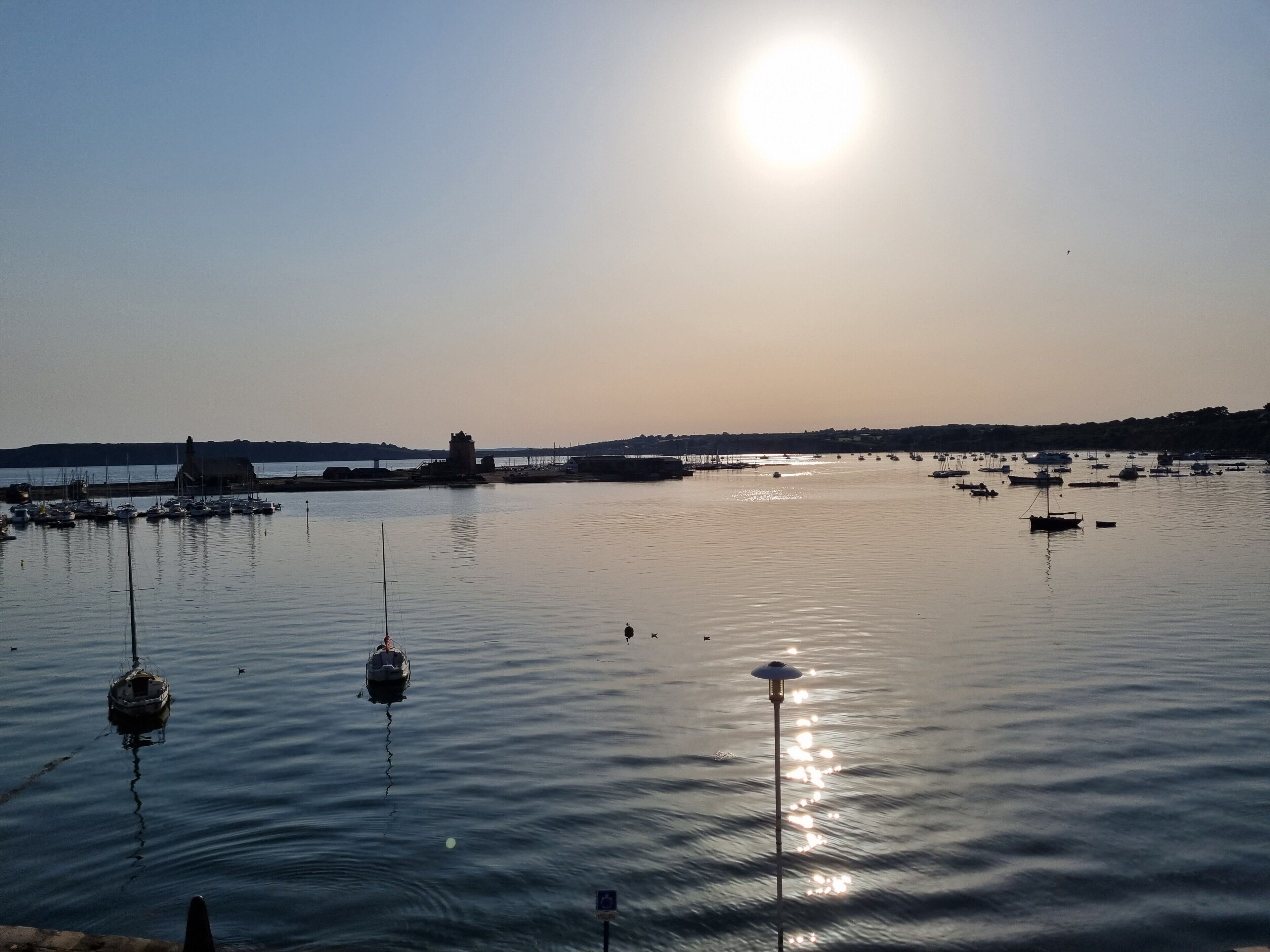 A calm harbor with boats, a lighthouse, and a distant shoreline.