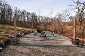 A gravel area with chairs and a fire pit, surrounded by trees and a wooden fence. - Jolly Acres | Hocking Hills, Luxury Cabin, Hot Tub (Logan)