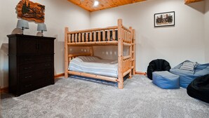 Ein Stockbett mit Holz Kopfteil, eine Kommode mit Lampen, ein blauer Sitzsack und ein gerahmtes Bild an der Wand.