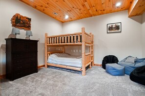 A bunk bed with a wooden headboard, a dresser with lamps, a blue bean bag, and a framed picture on the wall. - Jolly Acres | Hocking Hills, Luxury Cabin, Hot Tub (Logan)