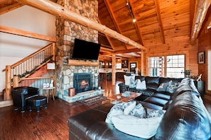 A spacious living room with a stone fireplace, leather furniture, and a wooden ceiling.