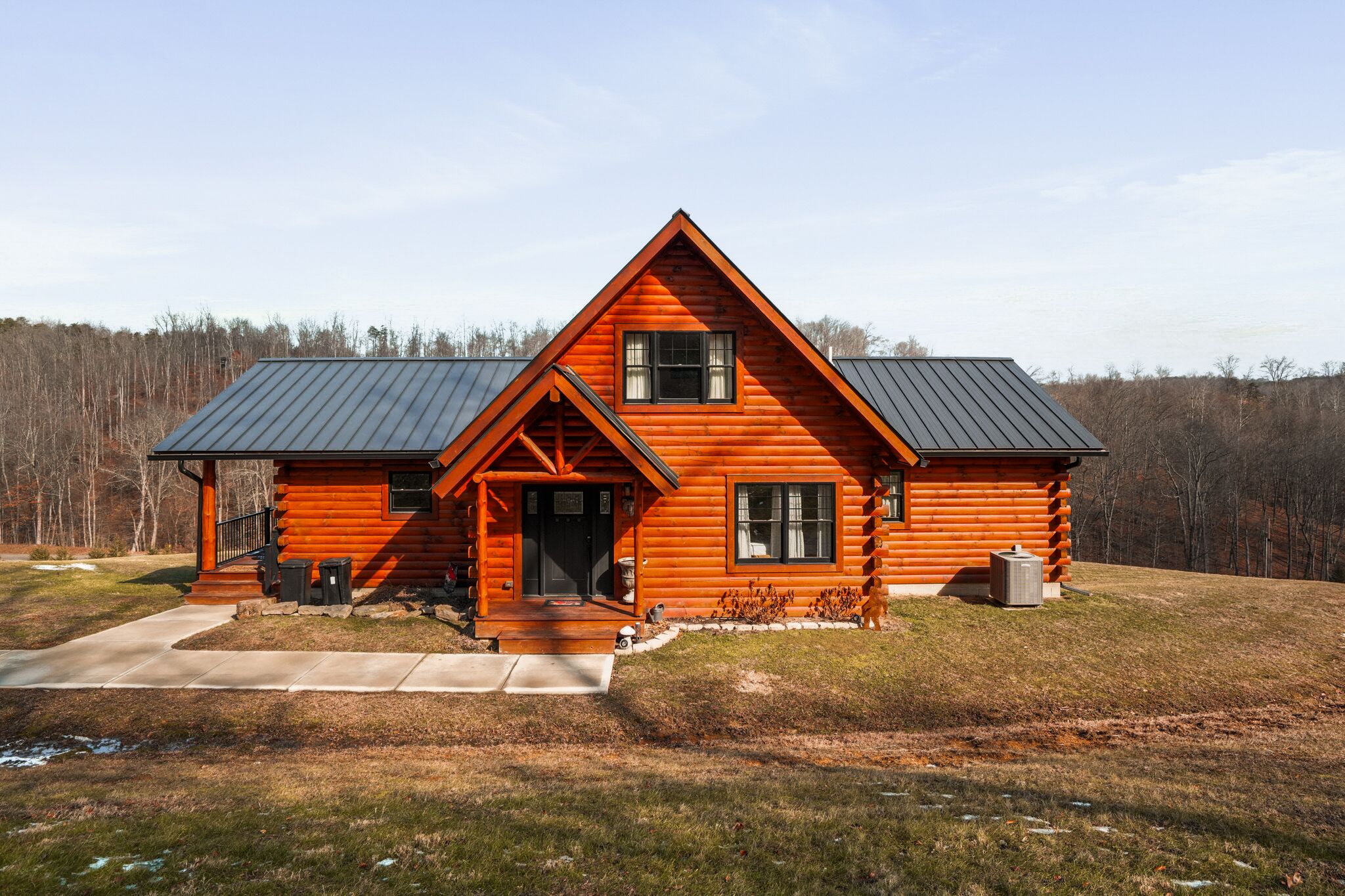 A log cabin with a metal roof, a front porch, and a small front yard.