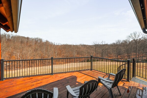 A wooden deck with outdoor seating and a view of a forested area.