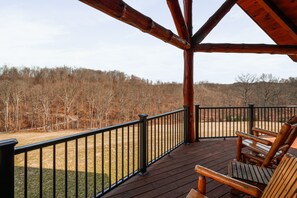 A wooden deck with a railing, a bench, and a view of a forested area. - Jolly Acres | Hocking Hills, Luxury Cabin, Hot Tub (Logan)