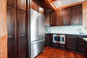 A kitchen with dark wooden cabinets, stainless steel appliances, and a white tiled backsplash. - Jolly Acres | Hocking Hills, Luxury Cabin, Hot Tub (Logan)