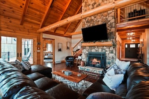 A cozy living room with a stone fireplace, leather sofas, and a wooden ceiling. - Jolly Acres | Hocking Hills, Luxury Cabin, Hot Tub (Logan)