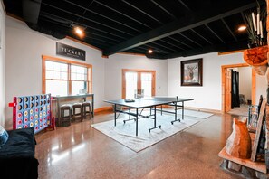 A spacious room with a ping pong table, a billiards table, and a dartboard.