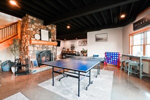 A ping pong table in a room with a stone fireplace, a staircase, and a bar/lounge area. - Jolly Acres | Hocking Hills, Luxury Cabin, Hot Tub (Logan)