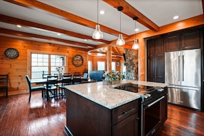 A kitchen with wooden beams, granite countertops, a stainless steel refrigerator, and a stone fireplace. - Jolly Acres | Hocking Hills, Luxury Cabin, Hot Tub (Logan)