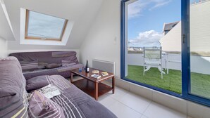 Una sala de estar moderna con techo inclinado, un ventanal grande, un sofá, una mesa de centro y vista a un patio trasero.