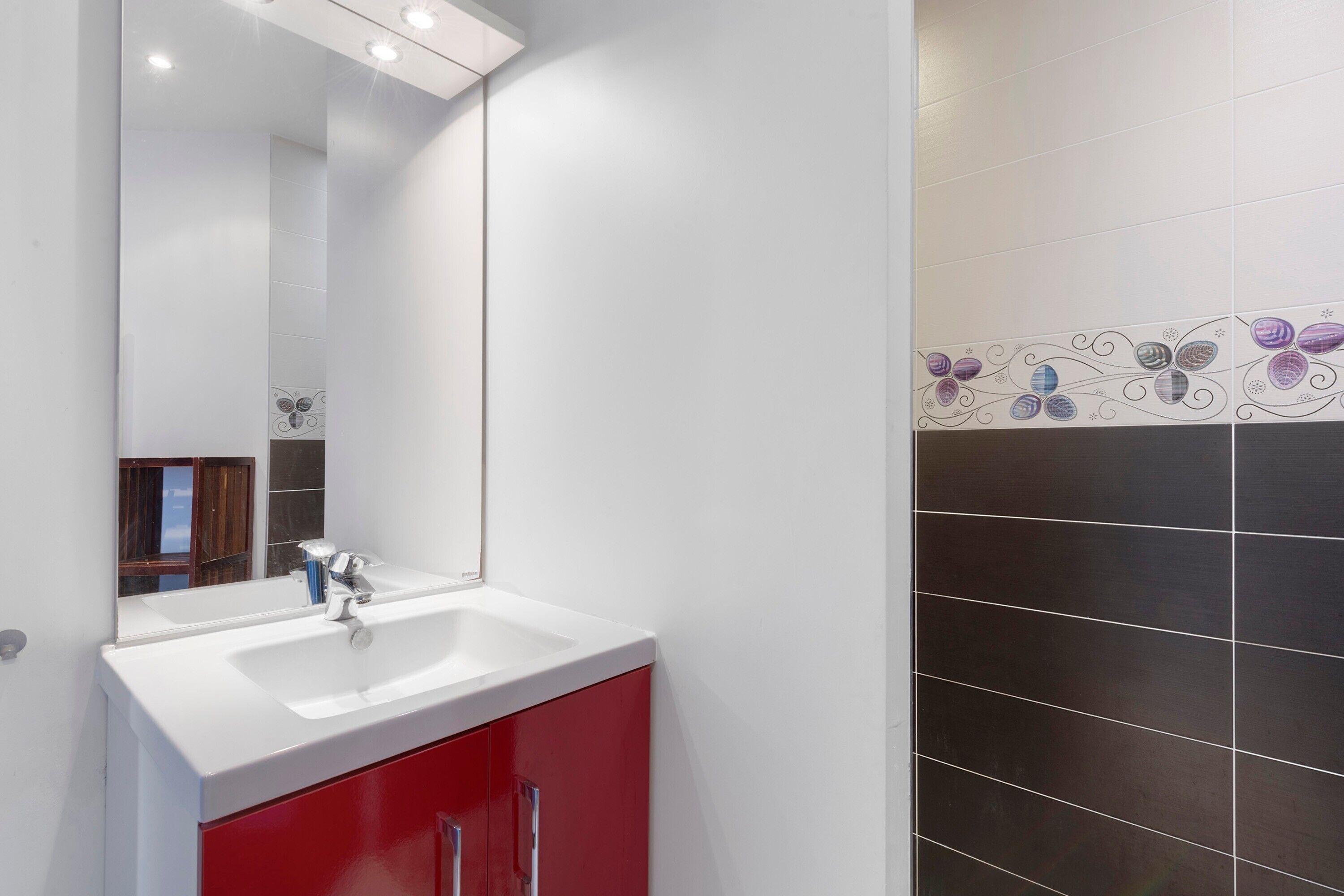 Une salle de bain avec un lavabo blanc, un meuble rouge et des carreaux décoratifs.