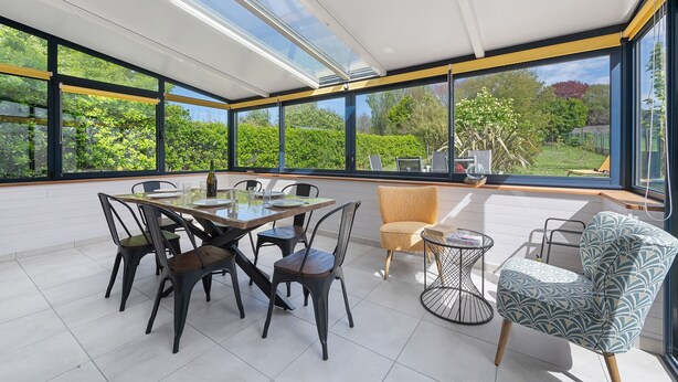 Ein moderner Essbereich mit einer gläsernen Veranda, einem Tisch mit Stühlen und einer Couch.