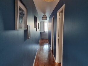 Un couloir aux murs bleus, doté d’un plancher en bois et orné de tableaux encadrés.